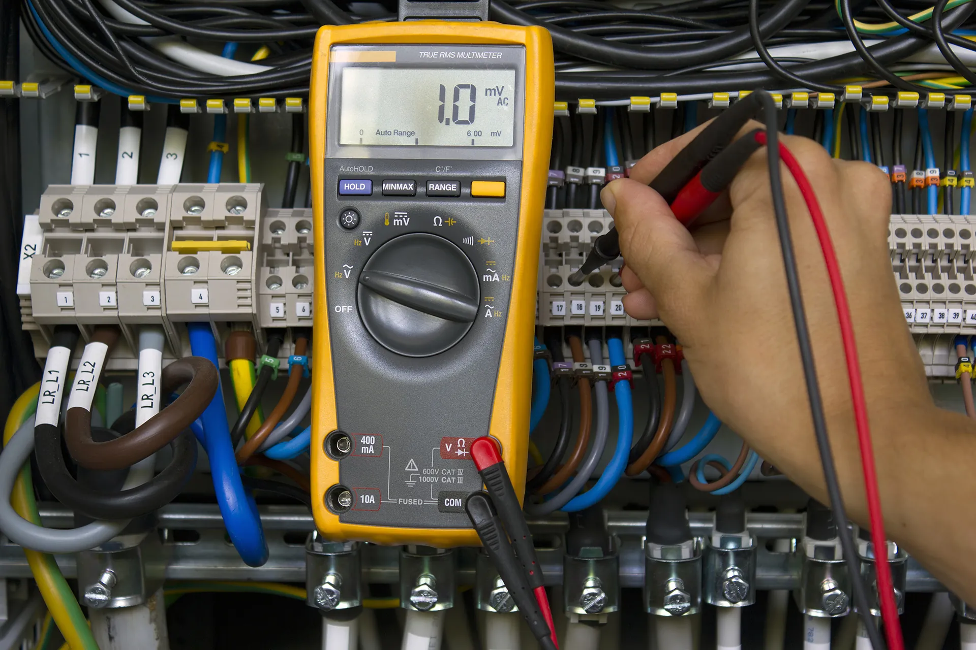 Electrician testing circuit breakers with a multimeter, illustrating our electrical guides
